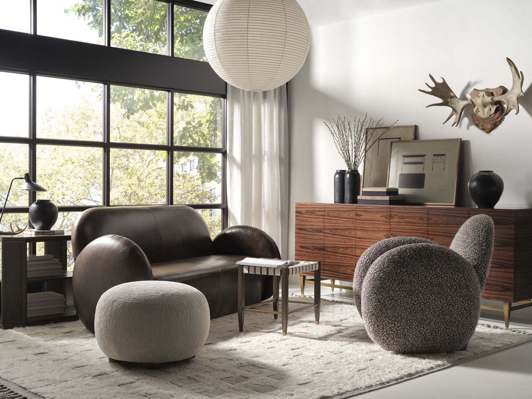 Rounded leather settee, round boucle pouf and swivel chair with a walnut credenza and brass accents, a curves, texture and mixed-materials look from Baker